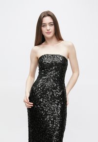 Juoda blizgi be petnešėlių suknelė su aptemptu siluetu, pasižyminti lygiu paviršiumi ir ilgu ilgumu, siekiančiu grindis.