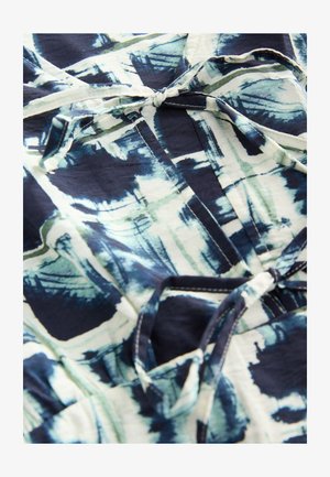 Jurk met patroon in marineblauw, groen en wit met een abstract ontwerp. Zachte stof met een strikdetail bij de halslijn en zichtbare stiknaden.