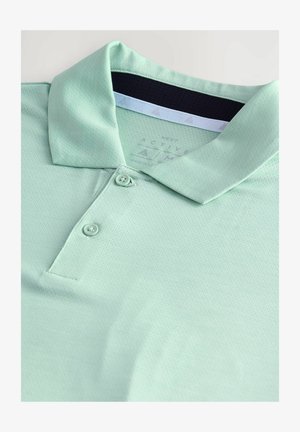 Polo verde chiaro realizzato in tessuto testurizzato, con collettino a tre bottoni e un'etichetta in tessuto sotto il colletto. Presenta un design traspirante.