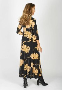 Długa czarna sukienka w kwiatowy wzór w odcieniach beżu. Sukienka ma rękawy do trzech czwartych oraz swobodny krój, zestawiona z czarnymi botkami za kostkę.