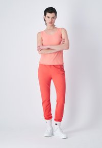 Coralowy top na ramiączkach i dopasowane dresowe spodnie z miękkiego materiału, cechujące się luźnym krojem. Białe trampki i skarpetki do kostek dopełniają sportowy wygląd.