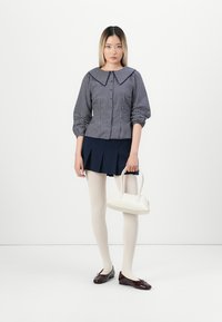Blusa a maniche puff a quadri blu e bianchi con ampio colletto, abbinata a una gonna plissettata blu, collant bianchi e una borsa bianca.