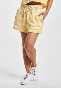 Kraťasy s tie-dye v žltej a bielej farbe, s elastickým pásom na šnúrku, bočnými vreckami a malým logom Nike na leme.