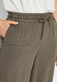 Elastische tailleband, strikdetail, schuin zak, gemaakt van zachte, lichte stof; in een gedempte olijf groene kleur met een subtiele textuur.