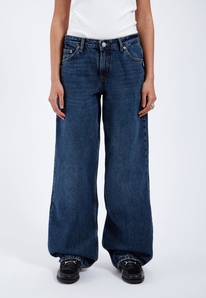 Vida jeans i mörkblå denim med vid ben, hög midja, femfickorsdesign, metallknappsstängning och kontrasterande sömmar.