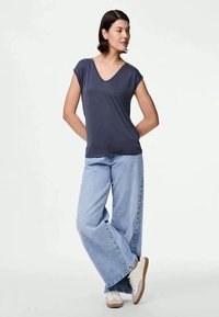 Dark navy V-neck t-shirt with short sleeves paired with light blue wide-leg jeans and white sneakers with brown soles.