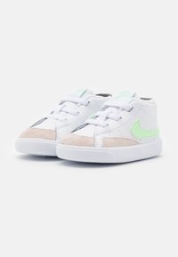 White sneakers with suede beige toe caps, green accents, and white laces. Textured rubber soles; low-top design with rounded silhouette.