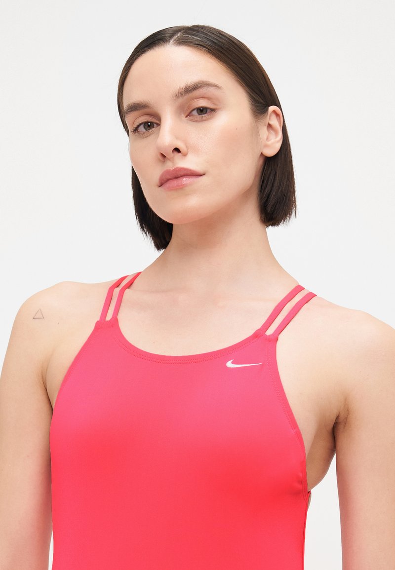 Top atlético rojo sin mangas con tirantes delgados y escote redondeado. Presenta un logo blanco de Nike en la parte superior izquierda. Textura suave.