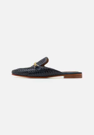 Scarpa slip-on in pelle nera intrecciata con tacco basso marrone e un accento decorativo in catena dorata sulla parte superiore. Fodera interna liscia.
