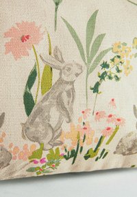 Szary królik wśród zielonych liści oraz różowych, żółtych i brzoskwiniowych kwiatów nadrukowanych na teksturowanej beżowej tkaninie.