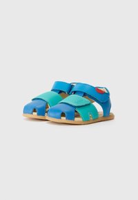 Blå og grønne skinnsandaler med åpne tær, justerbare stropper og en myk såle. Har et rødt element på siden.