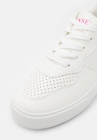 Hvide sneakers med en glat læderoverdel, perforeret tåområde, hvide snørebånd, struktureret gummisål og en lyserød detalje på tungen.