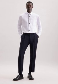 Wit overhemd met lange mouwen, voorzien van een zak en zwarte knopen, gecombineerd met op maat gemaakte marineblauwe broek en zwarte schoenen. Glad materiaal, gestructureerde pasvorm.