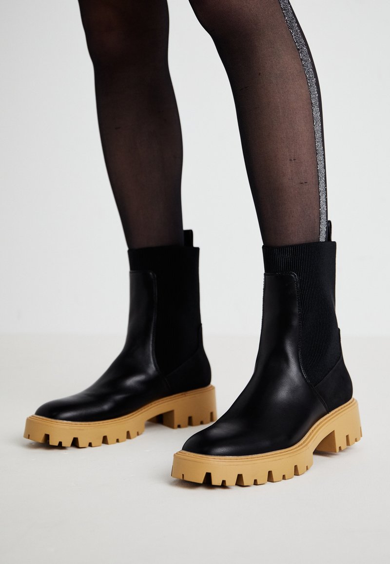 Sorte lær ankle boots med en chunky beige gummisål og ribbet tekstildetaljer. Glat overflade, rund tå og høj elastisk skaft.