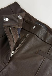 Pantaloni din piele ecologică de culoare maro, cu fermoar și închidere cu capse, precum și detalii de cusătură ajustată. Eticheta interioară a taliei este vizibilă.