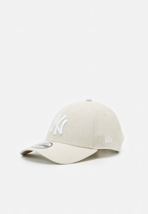 Casquette de baseball beige avec le logo des New York Yankees brodé en blanc sur le devant et une visière incurvée.