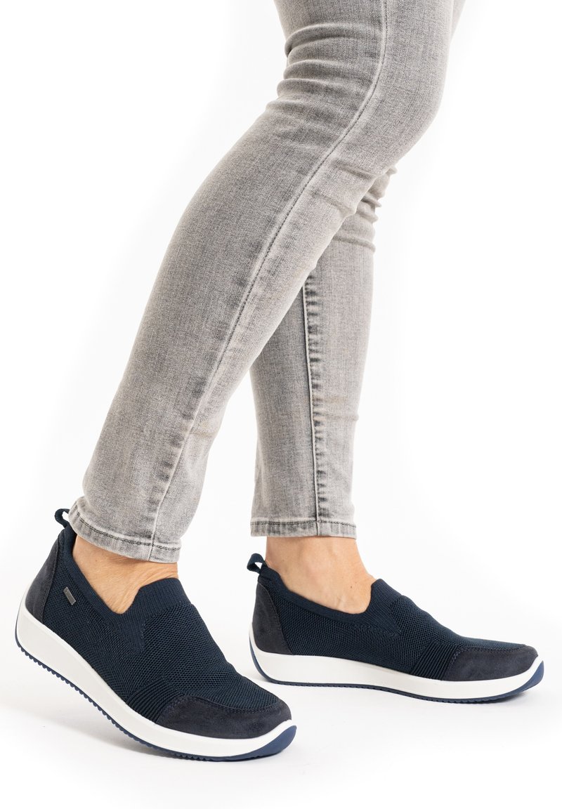 Navy slip-on shoes with breathable textile upper and suede accents. White rubber sole with traction pattern. Pairing with light grey jeans.