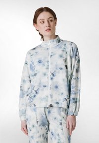 Jachetă cu imprimeu floral în albastru deschis și alb, având un guler înalt, închidere cu fermoar și manșete elastice. Material neted cu o croială lejeră.