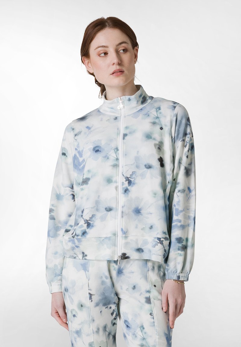 Jachetă cu imprimeu floral în albastru deschis și alb, având un guler înalt, închidere cu fermoar și manșete elastice. Material neted cu o croială lejeră.