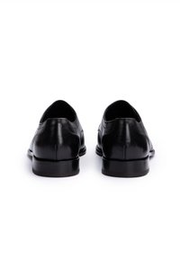 Scarpe nere in pelle con texture liscia, punta arrotondata, tacco basso e design minimalista. La vista posteriore mostra una silhouette elegante.