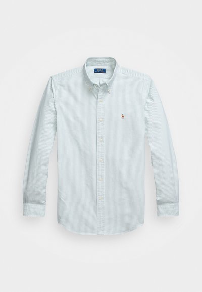 Camisa masculina de botão às riscas azul claro, com mangas longas, colarinho e um pequeno logótipo bordado no peito. Textura de tecido de algodão.