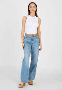 Vitt ärmlöst linne, ljusblå vida jeans, beige bälte och plattformssandaler. Slät tyg, avslappnad design och avslappnad passform på jeansen.