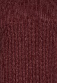 Tissu tricoté rouge foncé avec motif côtelé vertical, montrant une texture douce de laine et des détails de couture serrée.