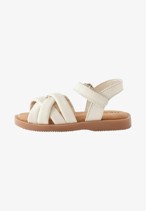 Sandali bianchi in pelle con cinturini incrociati e una cinghia alla caviglia sul retro. Soletta morbida marrone e suola in gomma testurizzata per una buona aderenza.