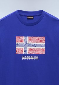 Modré bavlněné tričko s stylizovaným červenobílým designem norské vlajky, doplněné vlnovými vzory a textem "NAPAPIJRI geographic" pod ním.