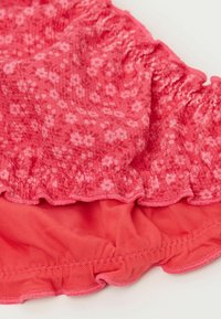 Tejido de color rosa con estampado floral, con bordes rizados y una capa inferior lisa y sólida. La textura parece suave, adecuada para ropa casual.