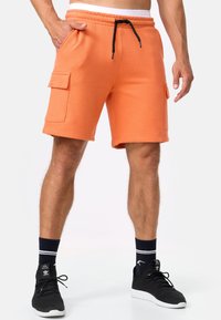 Shorts en coton orange avec une taille élastique et un cordon noir. Comprend deux poches latérales et des poches plaquées sur chaque cuisse.