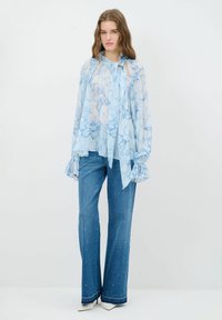Lyseblå blomstret bluse med lange ærmer og slipskrave, parret med blå denim flared bukser med udsmykning og subtil tekstur.