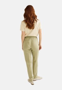 Pantalons légers et décontractés en lin vert sauge avec une taille élastique et deux poches arrière, associés à un haut crème.