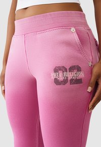 Różowe legginsy wykonane z miękkiej tkaniny, posiadają teksturowany pas, boczne przeszycia oraz nadrukowane logo z numerem na udzie.