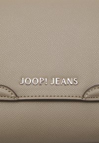 Borsa in pelle sintetica beige con superficie testurizzata. Presenta un logo argento "JOOP! JEANS" e accenti cuciti. Design rettangolare compatto.