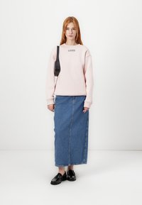 Felpa rosa chiaro con scollo rotondo e logo, abbinata a una gonna di jeans a vita alta e scarpe nere. Design minimalista.