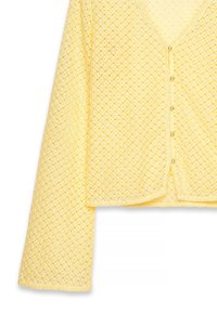 Gul strikket cardigan med v-hals og lange ærmer. Har et struktureret mønster og seks små perle-lignende knapper foran.