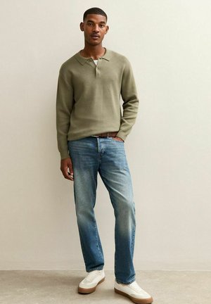 Suéter de punto verde caqui con cuello y detalle de botones, combinado con jeans de color azul claro y zapatillas blancas con suelas marrones. Diseño minimalista.