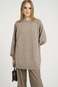 Jasnobrązowy, oversize sweter z raglanowymi rękawami, ściągaczami na mankietach i okrągłym dekoltem, zestawiony z szerokimi, beżowymi spodniami i małą torebką.
