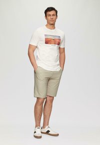 Camiseta blanca de manga corta con un gráfico de paisaje, combinada con pantalones cortos beige y zapatillas ligeras con acentos oscuros y una suela texturizada.
