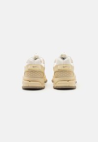 Tênis Nike Zoom em creme e bege com parte superior em malha e couro, calcanhar texturizado e um design de sola robusta que destaca características de estabilidade.