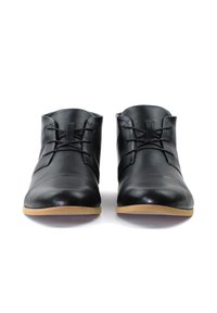 Botines de cuero negro con acabado suave, punta redondeada, cierre de cordones en la parte delantera y suela de goma marrón claro. Diseño atemporal y versátil.