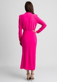 Różowa dopasowana sukienka midi z długimi rękawami i marszczonym pasem. Gładki, elastyczny materiał; zamek błyskawiczny z tyłu; rozkloszowany dół. Widoczne sandały na obcasie.