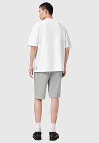 Άσπρο υπερμεγέθες μπλουζάκι με κοντά μανίκια, συνδυασμένο με γκρι σορτς μέχρι το γόνατο. Μαύρα παπούτσια και λευκές κάλτσες ολοκληρώνουν το ντύσιμο.