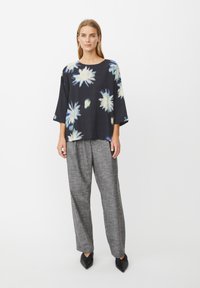 Sort bluse med blomster i lyseblå og hvide farver, afslappet pasform, 3/4-ærmer; kombineret med grå mønstrede bukser med vide ben og sorte spidse sko.