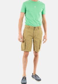 T-shirt verde in cotone, con logo sul petto, abbinata a pantaloni cargo beige con tasche laterali e vestibilità comoda. Scarpe casual incluse.