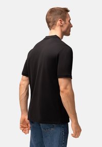 Černé bavlněné polo tričko s jednoduchým designem, krátkými rukávy a klasickým límcem, nošené s modrými džínami, zobrazené zezadu.