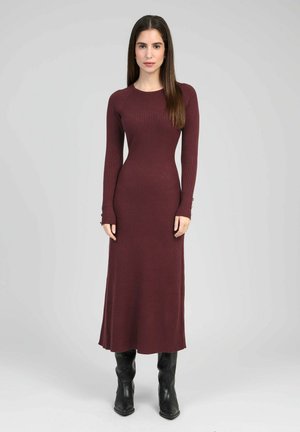 Longue robe côtelée bordeaux avec un corsage ajusté, des manches longues et un ourlet évasé, associée à des bottes noires montant jusqu'aux genoux.