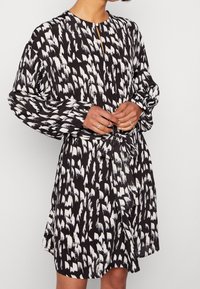 Svart och vit mönstrad klänning med långa ärmar, rund halsringning, knappstängning och knytband i midjan, tillverkad av lättviktsmaterial.