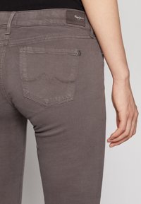 Jeans gris ajustados, fabricados en una mezcla de algodón, con un bolsillo trasero que presenta un patrón en zigzag y una etiqueta de cuero de marca en la cinturilla.